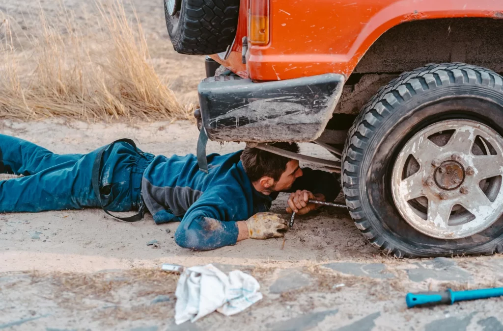 man lies under a 4x4 car on a dirt road